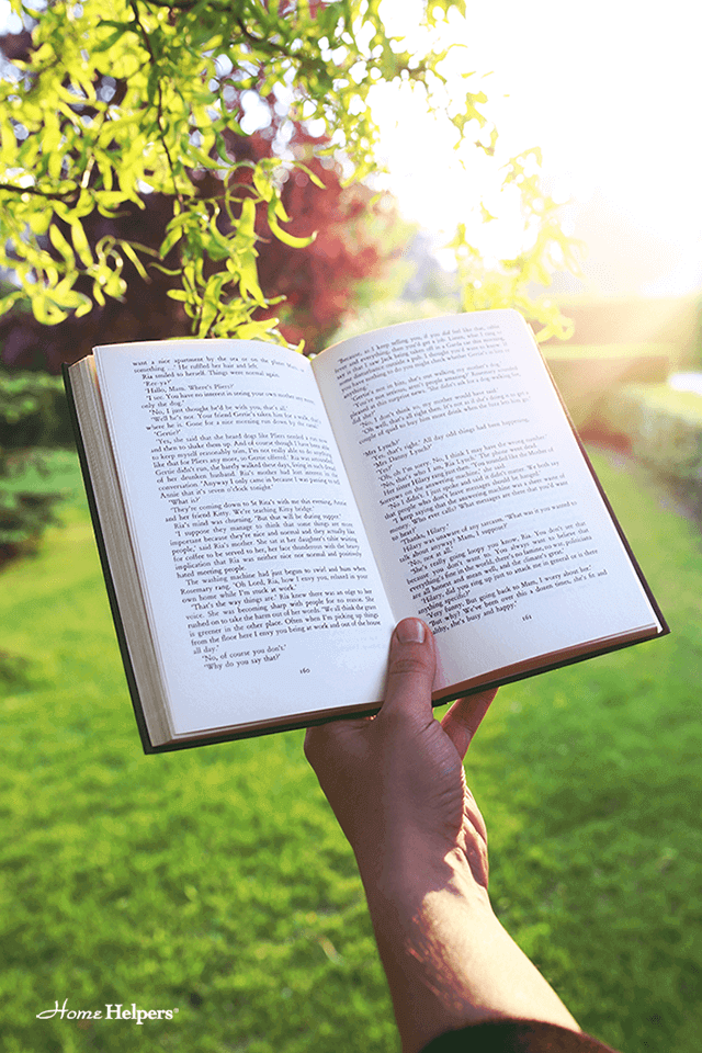 A person holding up an open book with trees and sunshine behind the book