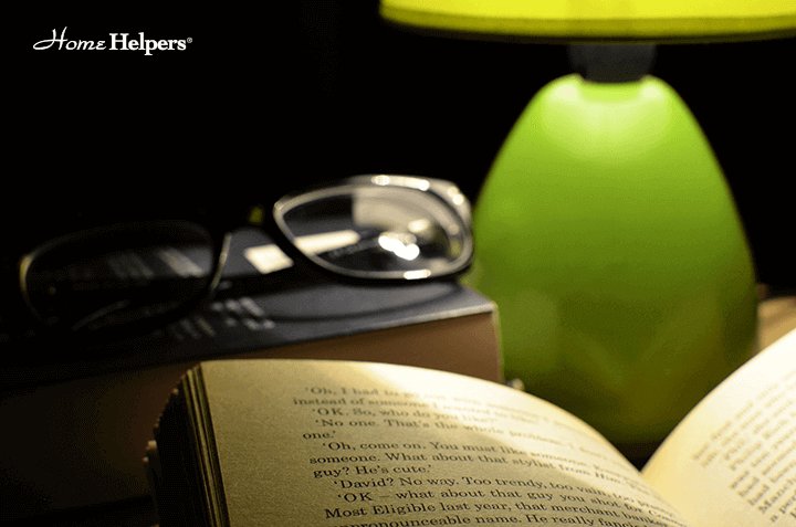 Close up of an open book on a table with reading glasses and a lamp
