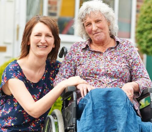 Woman smiling while sitting next to an elderly woman on a wheelchair