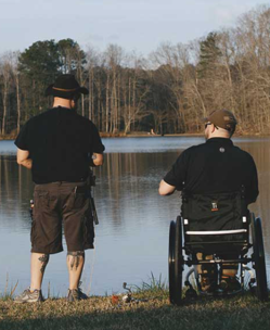One person standing one person in wheelchair by lake